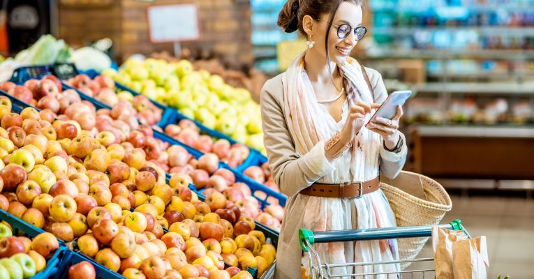 Frau mit Einkaufswagen im Supermarkt schaut auf Handy