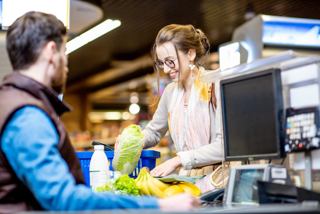 Männlicher Kassier und junge Frau an Supermarkt-Kasse mit Lebensmittel und Einkaufskorb