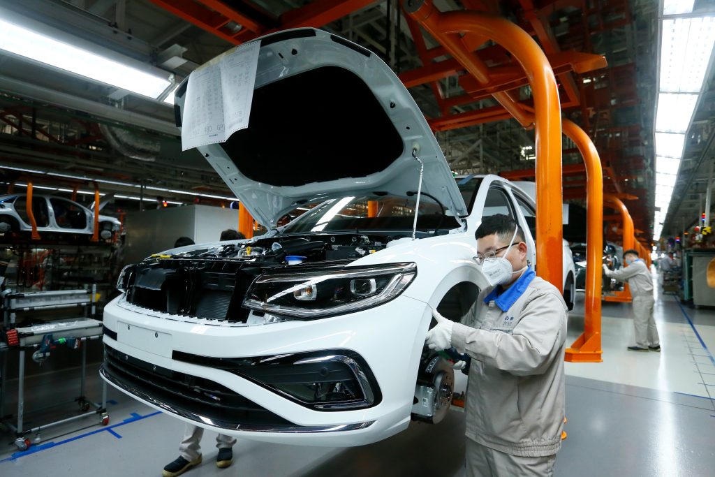 Asiate mit Schutzkleidung und Brille arbeitet an einem Auto in einer Fabrikhalle