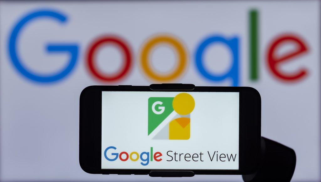 Handy, das Google Street View anzeigt und vor einer großen Wand mit der Aufschrift Google ist