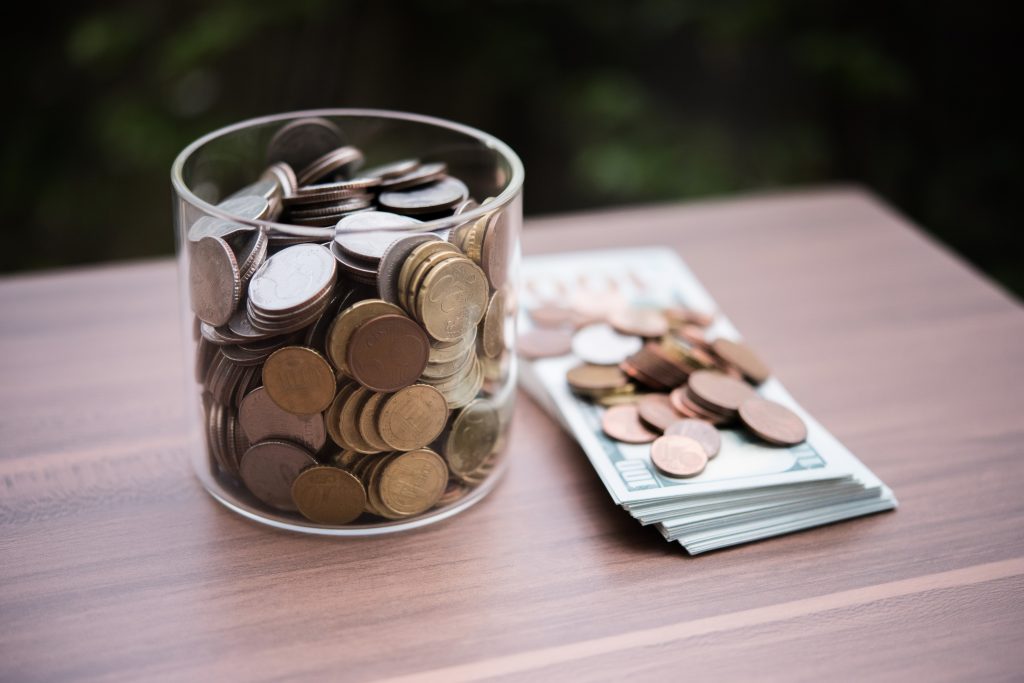 Münzen in einem Glas und Münzen die auf Geldscheinen liegen