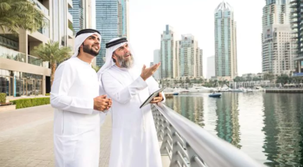 Zwei Scheichs mit weißer Kleidung und weißer Kopfbedeckung stehen an einem Fluss in Dubai und schauen Richtung Himmel