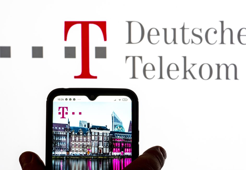 Logo der Deutschen Telekom auf weißem Hintergrund davor ein Handy das eine Häuserfront zeigt und auch das Logo der Deutschen Telekom