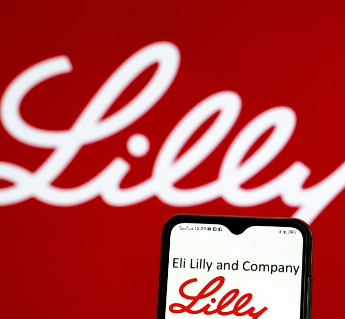 Logo von Lilly in rot davor ein Handy das Eli Lilly Company am Display zeigt und darunter wieder den Schriftzug von Lilly in rot
