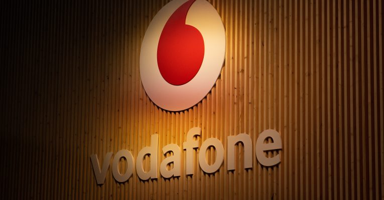 Logo von Vodafone auf einer Holzwand. Darüber ein rotes Anführungszeichen in einem weißen Kreis