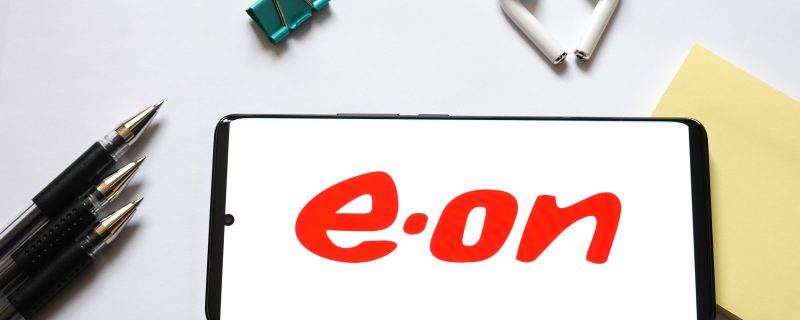 Weißer Hintergrund auf dem ein Kugelschreiber, eine Klemme und zwei Ohrenstoppel sowie ein Post-it zu sehen sind. Davor ein Handy, dass das Logo von E.ON am Display zeigt