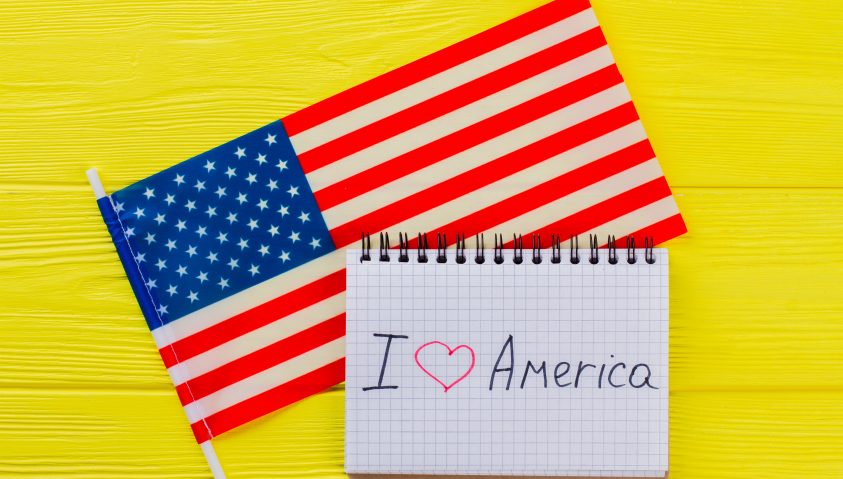 Flagge der USA mit kleinem Kalender davor mit der Aufschrift I love Amerika. Beides auf gelben Hintergrund