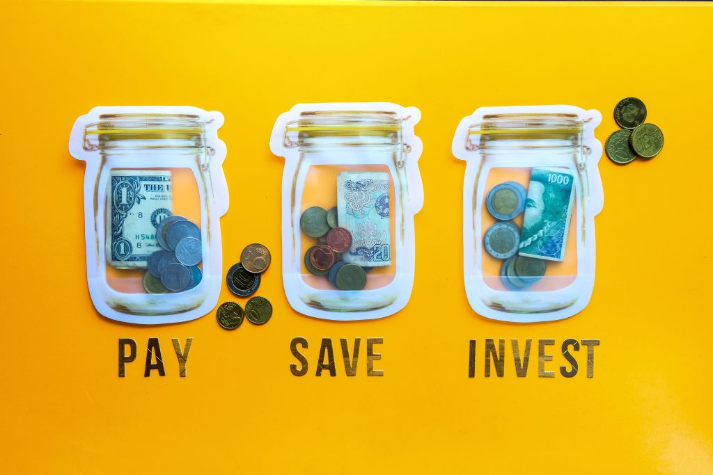 Drei Gläser stehen nebeneinander auf gelben Hintergrund und sind mit Geld gefüllt. Darunter stehen unterschiedliche Wörter wie 