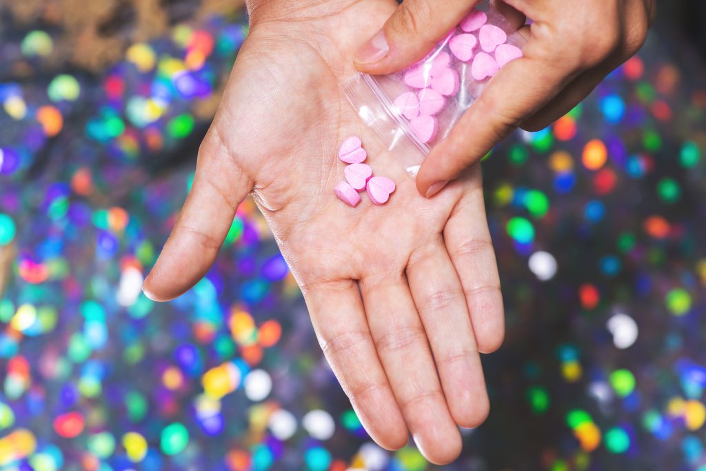 Partykonfetti und zwei Hände, die ein Säckchen voller Herz-Pillen halten