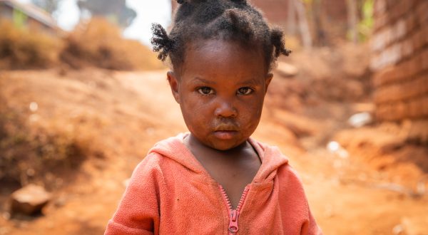 Armes kleines Mädchen in dreckiger Kleidung in einem afrikanischen Dorf, Armuts- und Krisenkonzept.
