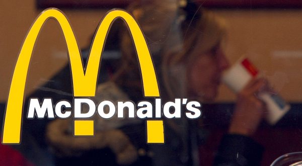 Logo einer McDonald's-Filiale. Hinter dem Fenster sitzt eine Frau.