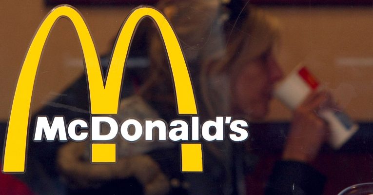 Logo einer McDonald's-Filiale. Hinter dem Fenster sitzt eine Frau.