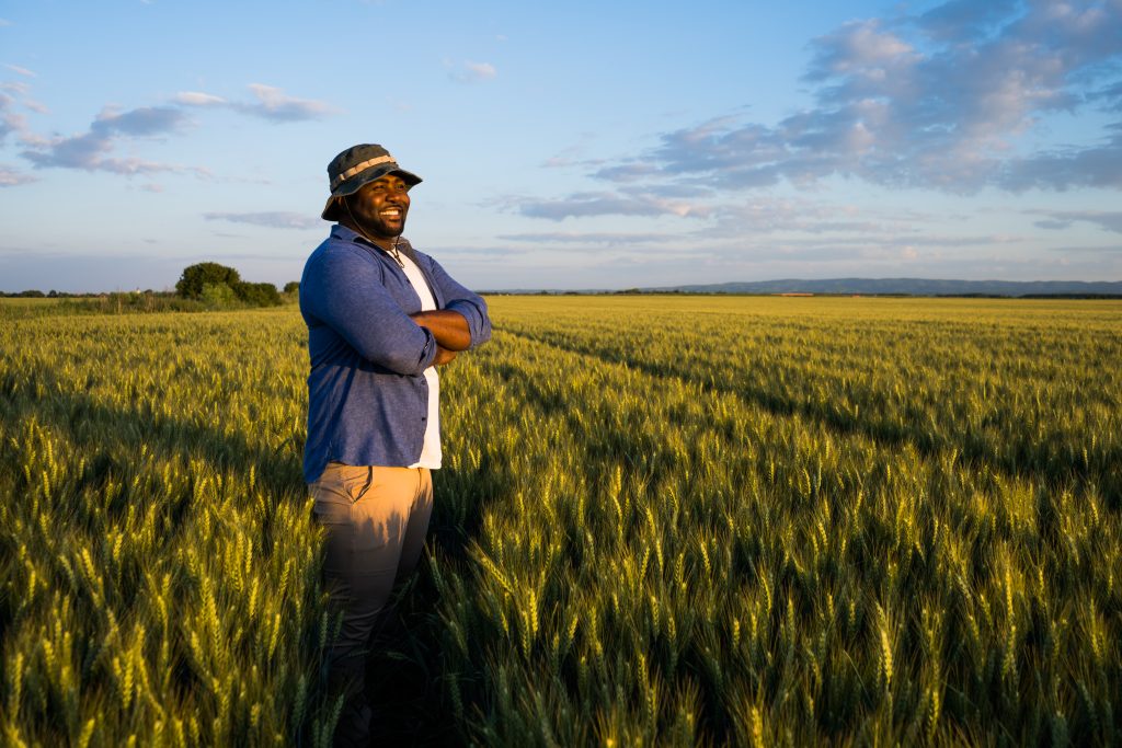 Afrikanischer Bauer steht auf einem Weizenfeld und lächelt