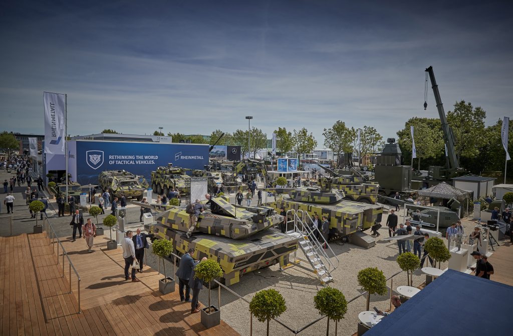 Verschiedene Panzer auf einem Gelände mit Besuchern. Dahinter ein großes Plakat in blau der Rheinmetall