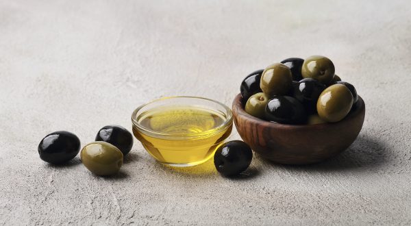 Oliven liegen neben einem kleinen Schälchen Olivenöl