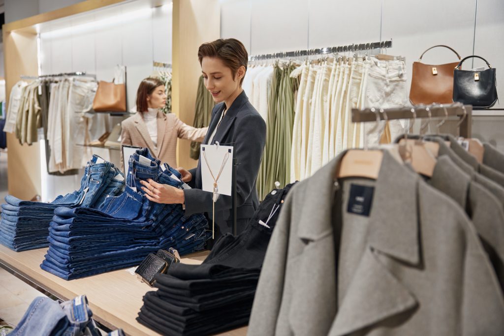 Frau hält eine Jean auf einem Stapel in einem Geschäft in die Höhe