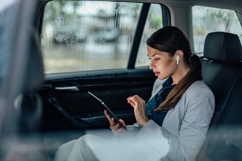 Junge Frau sitzt mit einem Tablet in eine Auto