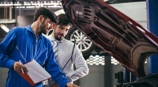 Zwei Mechaniker stehen vor einem Auto bei dem die Motorhaube geöffnet ist