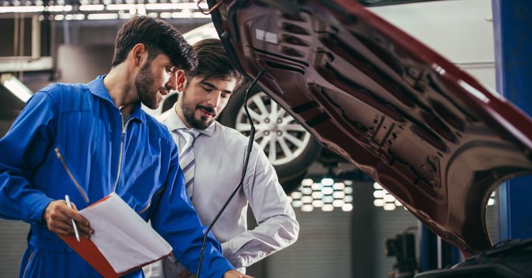 Zwei Mechaniker stehen vor einem Auto bei dem die Motorhaube geöffnet ist