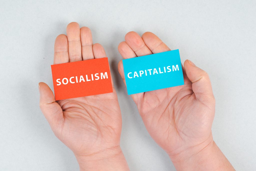 zwei Hände mit rot Socialism und blau Capitalism Karten in der Hand